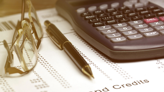 An image of a calculator, reading glasses and pen sitting on top of tax and credits documents; for blog post about employee retention (ERC) claims